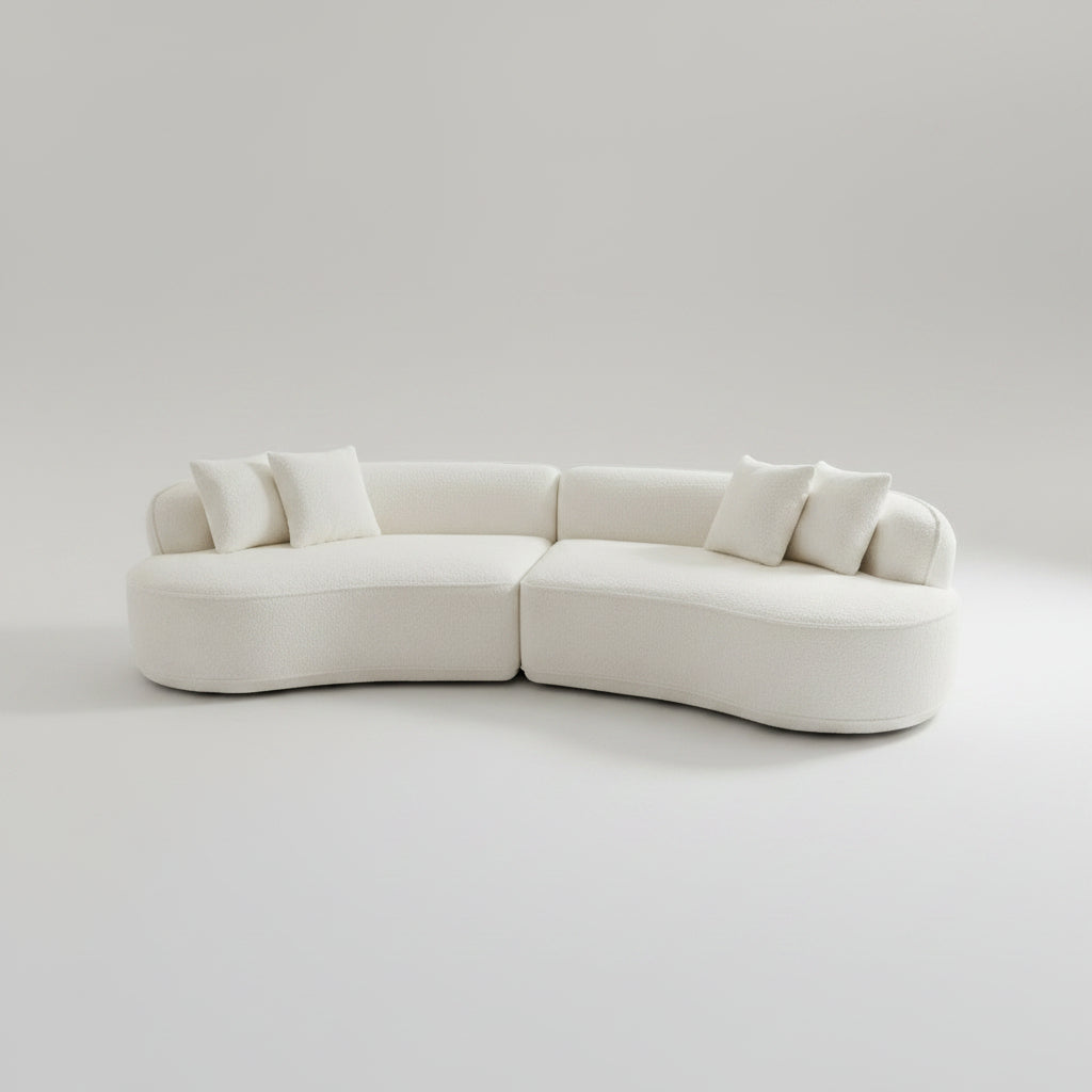 A modern curved modular sofa upholstered in off-white fabric, featuring several matching throw pillows, set against a seamless light gray studio background.