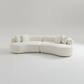 A modern curved modular sofa upholstered in off-white fabric, featuring several matching throw pillows, set against a seamless light gray studio background.