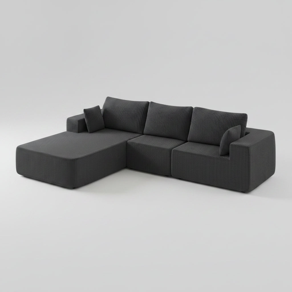 A dark gray ribbed fabric sectional sofa with a chaise lounge, styled in a warm, modern living room with a beige rug, wooden floor, and wall decor.