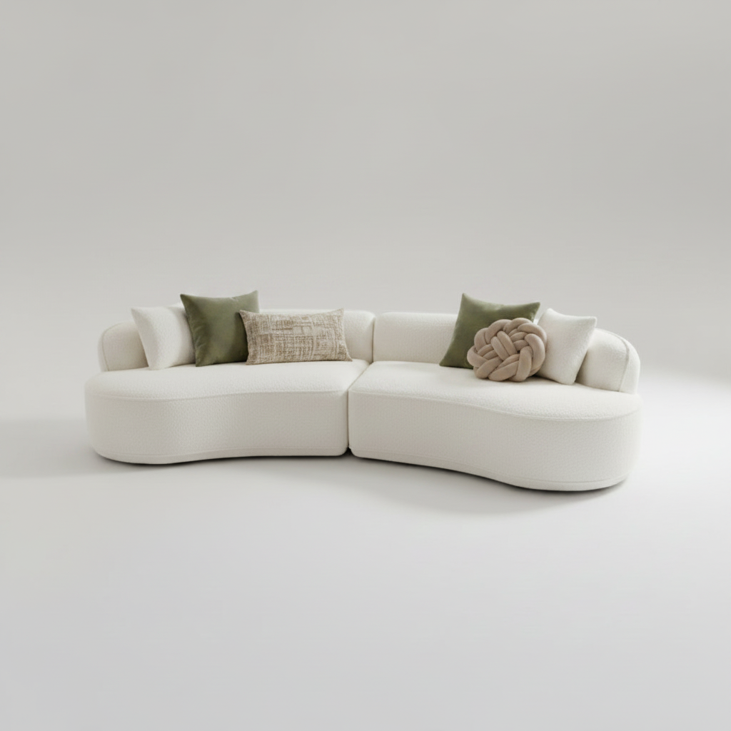 A modern curved modular sofa upholstered in a soft off-white fabric, accented with four matching square throw pillows, set against a seamless light gray studio background.